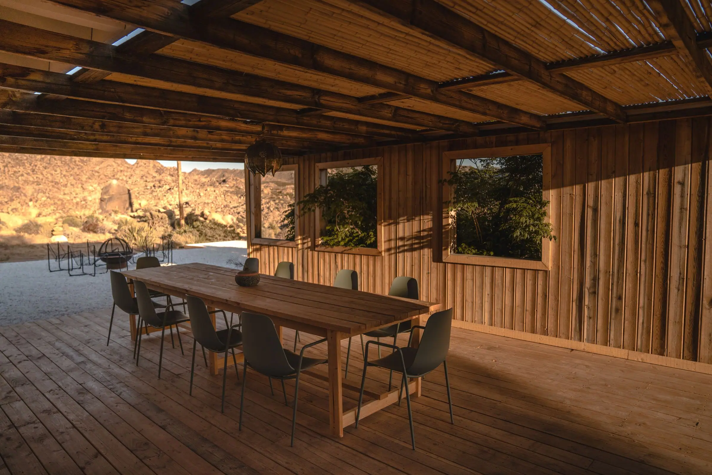 Wood covered deck with a long dining table and desert hills behind