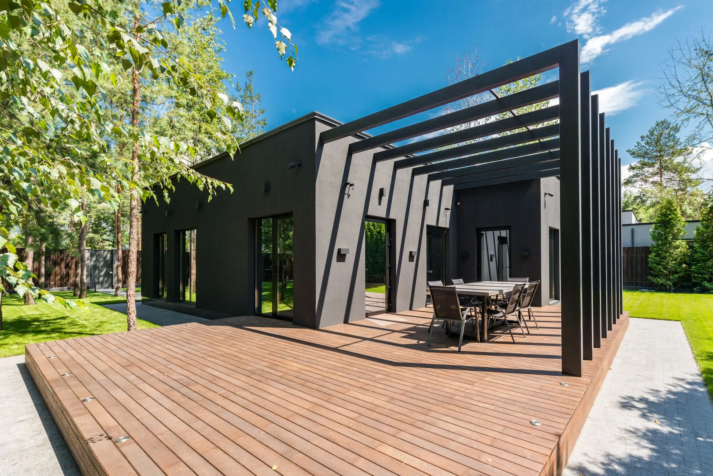Freestanding black pergola over a wood deck and dining set