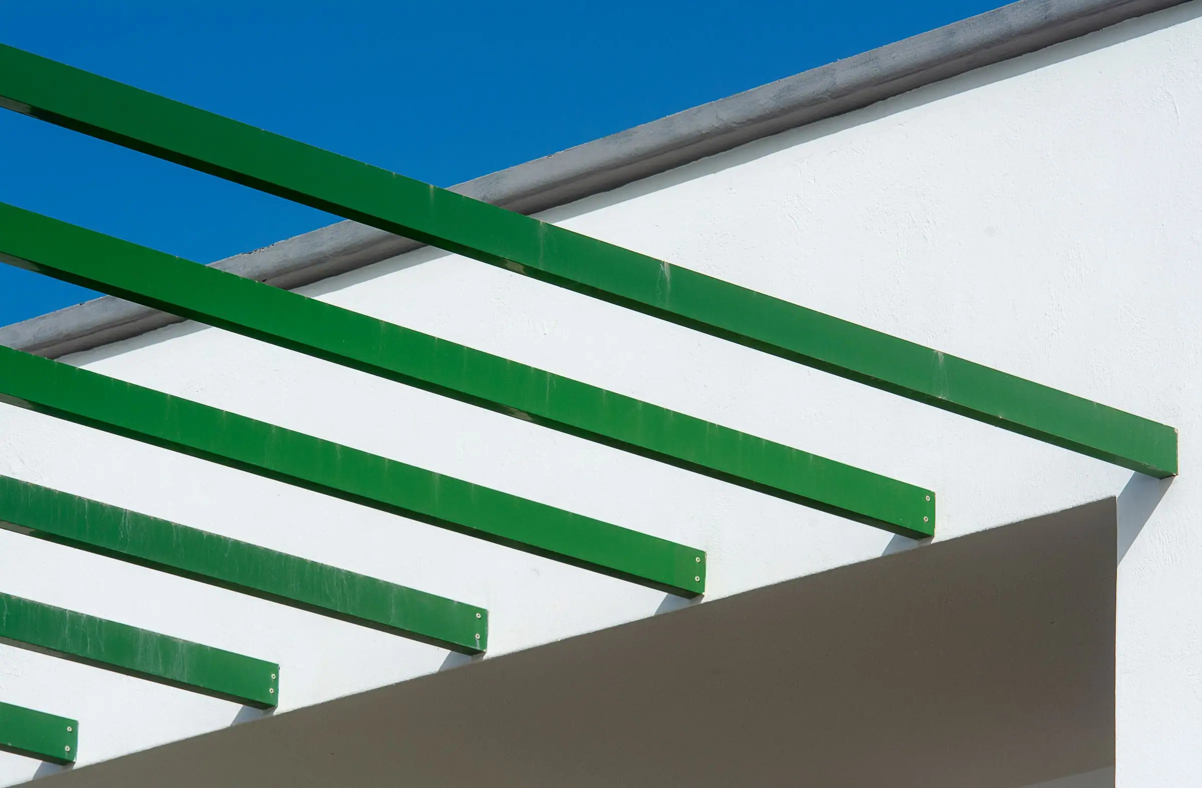 Green pergola beams against a clear blue sky