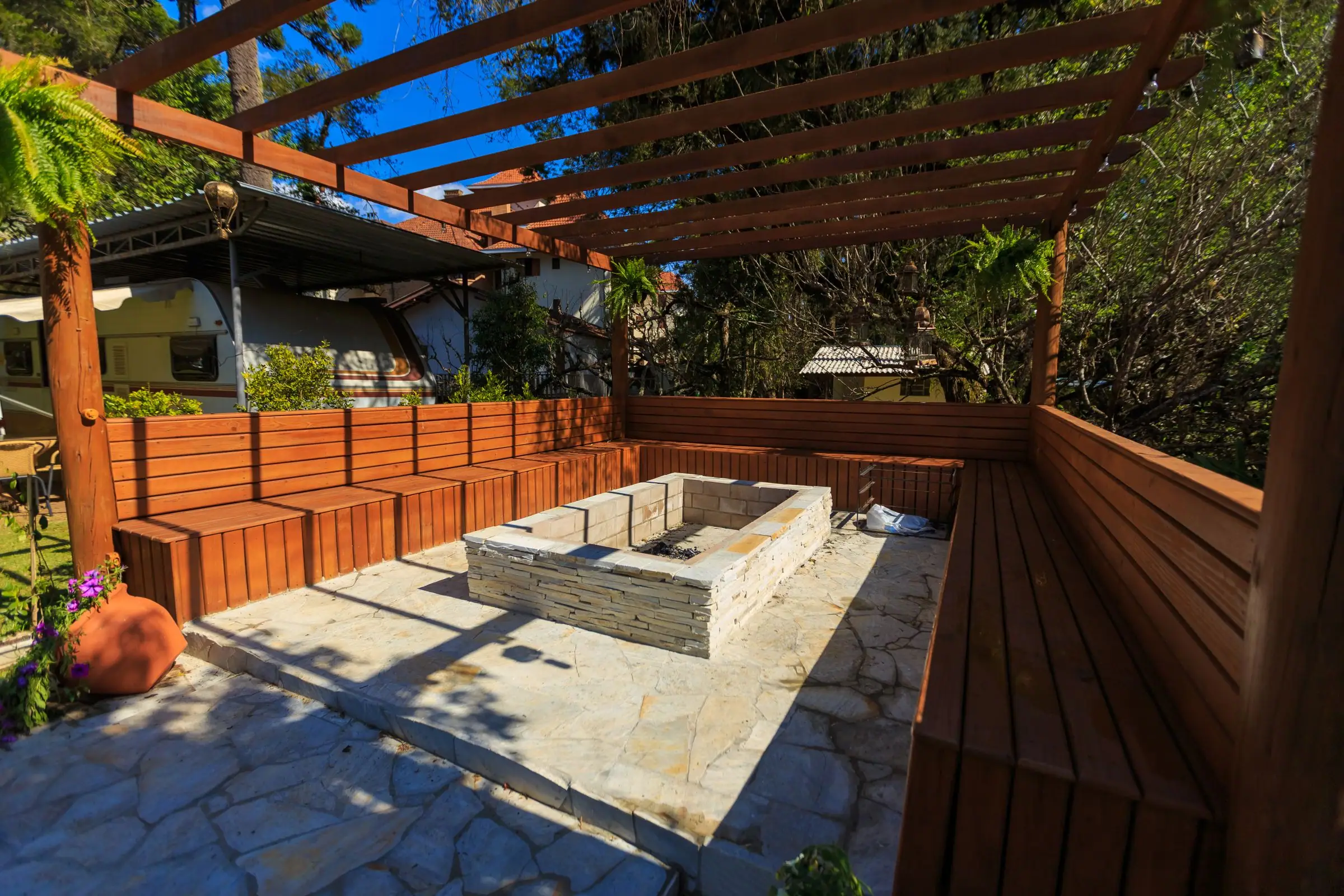 Wood pergola over built-in benches and a stone fire pit
