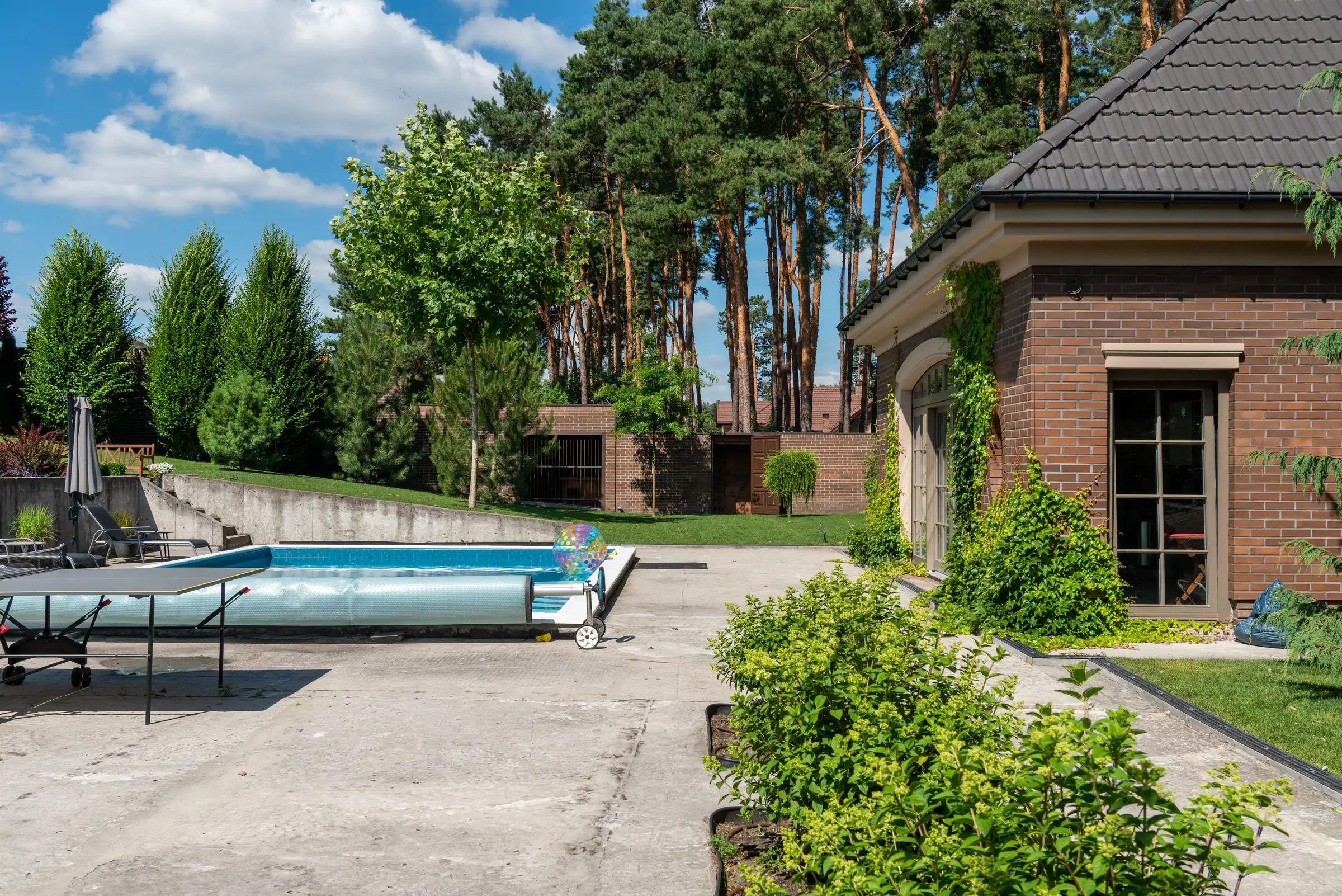 Backyard pool with a concrete deck and a table tennis table beside a brick house