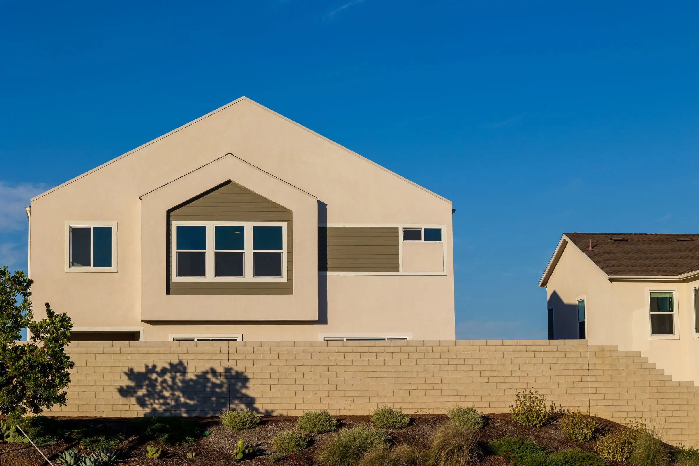 Tan stucco home behind a block wall under a deep blue sky
