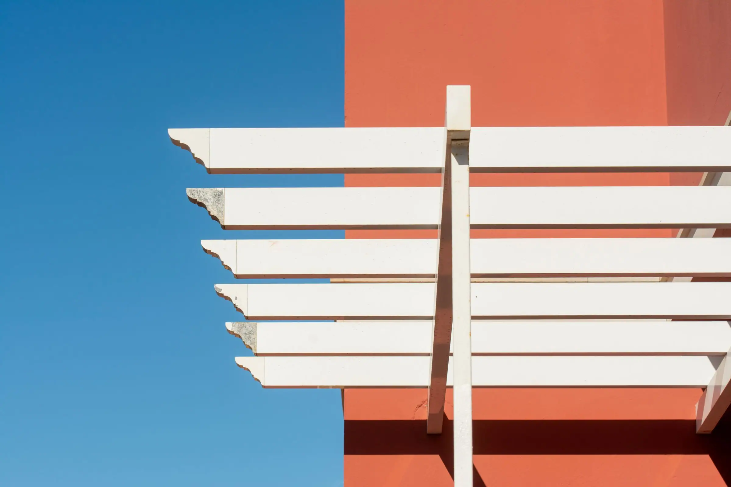 White pergola slats against an orange stucco wall